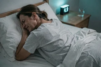 Femme allongée dans son lit la nuit souffrant de douleurs au dos contracté, vue de dos en gros plan