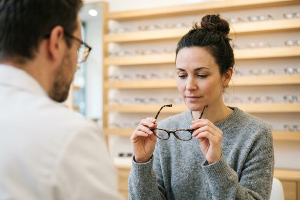 Femme en train d'essayer une nouvelle monture de lunettes chez un opticien, tenant les lunettes dans ses mains avec une expression réfléchie